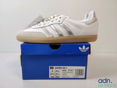 une paire de baskets Adidas blanches posées sur une boîte bleue