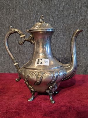 une théière ancienne en argent, munie d'une anse, posée sur une nappe rouge
