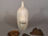 un vase blanc orné d'un visage, à côté de trois autres objets