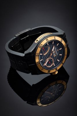 the black and gold watch is sitting on a black surface