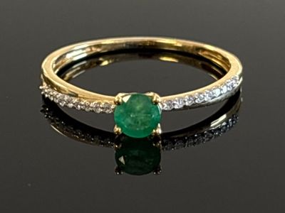 a close up of a green emerald and diamond ring on a black surface