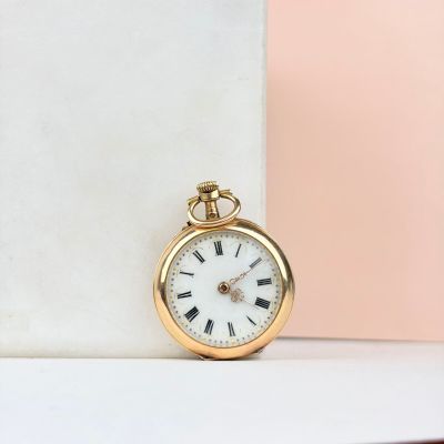 montre de poche en or avec des chiffres romains, posée sur un bloc de marbre