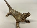 an old bronze lizard figurine sitting on a white surface
