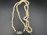 un collier de perles blanches muni d'un fermoir en argent, posé sur un fond noir