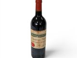 une vieille bouteille de vin rouge posée sur une surface blanche
