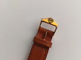 the brown leather watch strap has a gold buckle on it