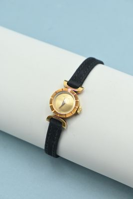 une montre en or avec un bracelet noir posée sur une serviette