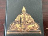 un livre posé sur une table en bois, à côté d'une statue de Bouddha dorée
