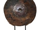 une image représentant un grand gong en bois posé sur un socle, sur fond blanc