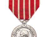 Gros plan sur une médaille sur fond blanc, accompagnée d'un ruban rouge