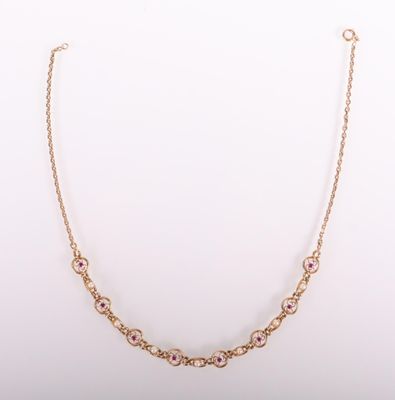 un collier en or orné de pierres roses sur fond blanc