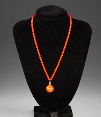an orange beaded necklace with a pendant on a black mannequin