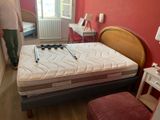 un homme debout à côté d'un lit sur lequel est posé un matelas