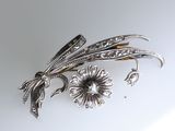 a silver brooch with flowers and leaves on it
