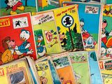 a pile of comics on a table with a person holding a cell phone