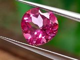 un gros plan d'un diamant rose tenu par une paire de pinces