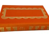 an orange book with a gold border on top of it