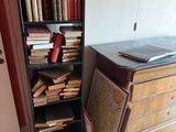 a book shelf with many books on it next to a chest of drawers