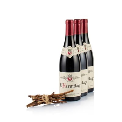 three bottles of red wine sitting next to a bundle of sticks