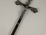 une croix en métal munie d'un manche en bois, posée sur une table