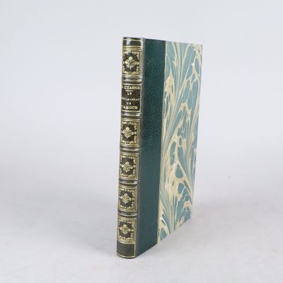 un livre vert aux bords dorés posé sur une surface blanche