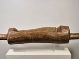 sculpture représentant une main en bois tenant un tube en bois, posée sur un socle blanc
