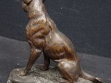 bronze statue of a dog sitting on a rock on a black background