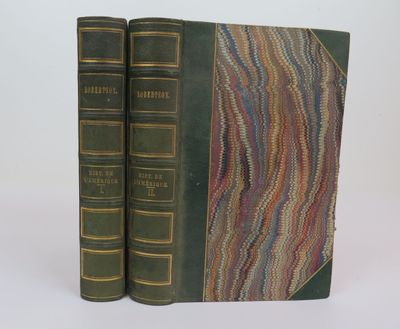 two books are sitting on a white surface, one is green and the other is brown