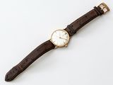 a close up of a watch on a white surface with a brown strap