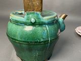 a green teapot with a wooden lid sitting on a table