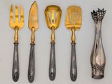 four silver and gold utensils are lined up on a white surface