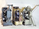 trois vieux projecteurs de cinéma posés les uns à côté des autres sur une surface blanche