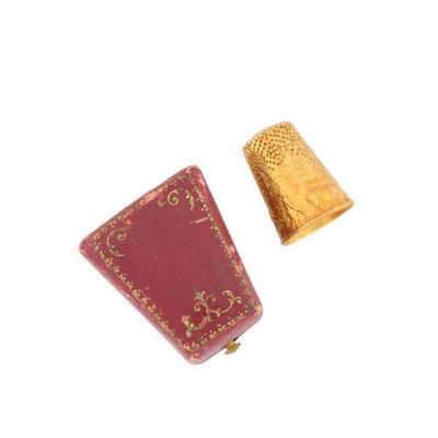 un dé à coudre doré et un livre rouge posés sur une surface blanche