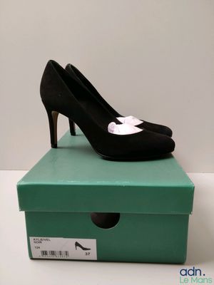 des chaussures à talons hauts noires et blanches posées sur une boîte verte, elle-même posée sur une surface blanche