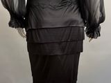 a woman ' s black dress with sheered sleeves and ruffled skirt