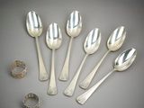 six silver spoons and a ring on a gray surface