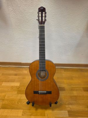 an acoustic guitar sits on a stand on a hard wood floor