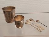 une coupe en argent, des cuillères et un repose-cuillères posés sur une table en verre