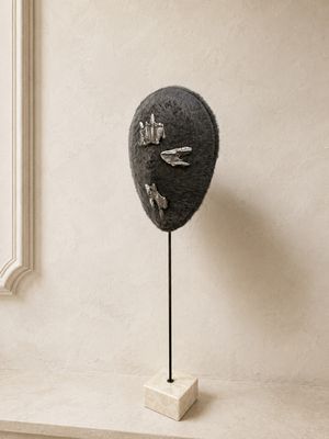 une sculpture représentant un visage, posée sur un socle devant une fenêtre