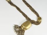 a close up of a gold necklace with a tassel on a white surface