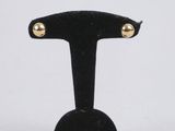 une paire de boucles d'oreilles cloutées de couleur dorée, posées sur un socle en velours noir