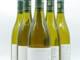 quatre bouteilles de vin blanc sont alignées sur une surface blanche