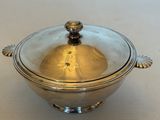une cocotte plaquée argent avec un couvercle en verre, posée sur une table blanche