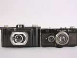 two old cameras sitting side by side on a white surface