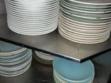 many plates stacked on a metal shelf in a kitchen
