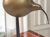 a bronze bird on a wooden table in front of a window
