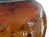 a brown vase with red flowers in it on a white surface
