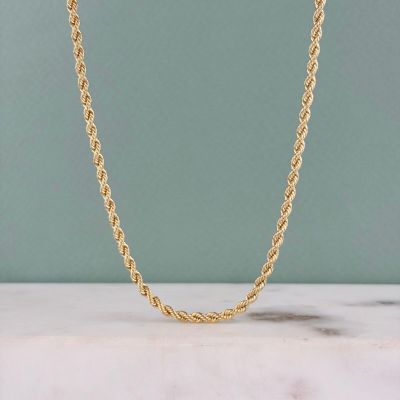 un gros plan d'un collier à chaîne en or posé sur une surface en marbre