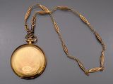 a gold pocket watch with a chain on a gray surface