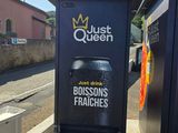 une affiche sur le bord de la route sur laquelle on peut lire « Just Queen, Just Drink Boissons Fraîches »